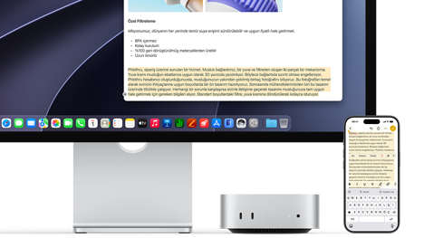 Mac mini’nin önden görünümü, Studio Display’in altına yerleştirilmiş, aygıtın ve ekranın sağ tarafında bir iPhone duruyor, iPhone’da seçili metnin üzerinde kes, kopyala, yapıştır ve AutoFill komutları görülüyor ve seçili metnin aynısı ekranda da gösteriliyor, Evrensel Pano özelliği vurgulanıyor